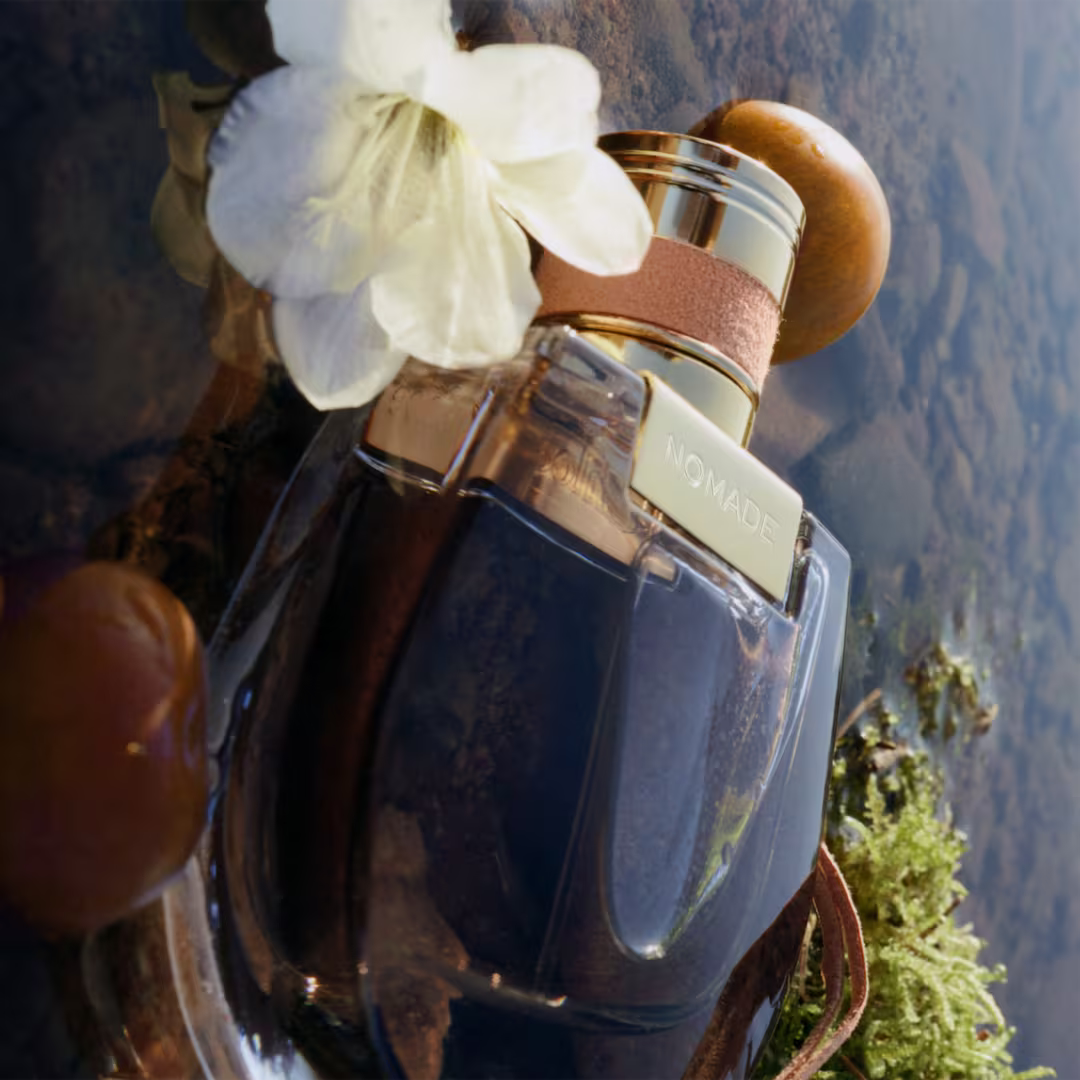 Chloé Nomade EDP bottle with white flower and leather cord in outdoor mountain setting lifestyle shot